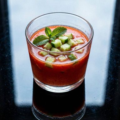 Wassermelonen-Gazpacho Erfrischende rote Wassermelonen-Gazpacho in einem Glas, garniert mit feinen Gurkenwürfeln und frischen Minzblättern.
