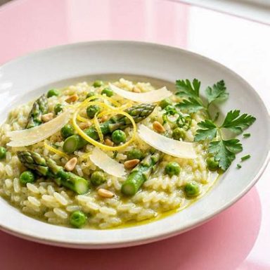 Cremiges grünes Risotto mit Spargelstücken, Erbsen, Zitronenabrieb und Parmesan, serviert mit Pinienkernen und frischen Kräutern.